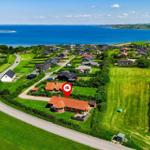 Haus mit rotem Dach liegt an einer Straße neben Grünflächen und einem See.