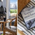 Ein Raum mit Sitzgelegenheiten und Blick auf die Außenterrasse. Ein Buch liegt auf einem gestreiften Kissen.