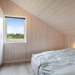 Schlafzimmer mit Holzwand, Bett und Fenster mit Blick auf Grünflächen.