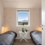 Zimmer mit zwei Betten, Holzwand und Fensterblick auf Dach und Gras.