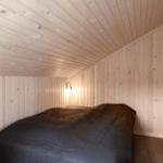 Schlafzimmer mit Holzwandverkleidung und Bett mit dunkler Bettwäsche.