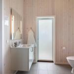 Bad mit Waschbecken, Toilette und Dusche. Holzwand und Spiegel sichtbar.