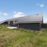 Ein dunkel verkleidetes Ferienhaus mit Terrasse und Picknicktisch in einer grünen Landschaft.