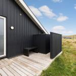 Schwarzes Holzhaus mit Terrasse und Sitzbank im Grasland.
