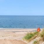 Strand mit Sand, Dünen und blauem Meer. Rettungsboot steht am Ufer.
