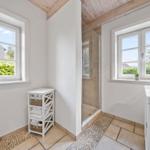 Badezimmer mit Dusche, Waschbecken und Fenstern. Holzdecke und Fliesenboden.