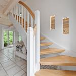Treppenhaus mit Holzstufen und weißem Geländer. Im Hintergrund steht ein weißer Schrank und ein Fenster.