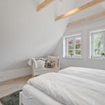 Zimmer mit zwei Betten, Holzbalken an der Decke und Fenstern mit Blick auf Bäume.