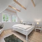 Schlafzimmer mit Dachschrägen, zwei Fenstern, Bett, Nachttisch und Schrank.