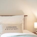 Ein Bett mit Kissen, das die Koordinaten von St. Peter-Ording zeigt.