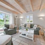 Wohnzimmer mit grünen Sitzmöbeln, weißem Couchtisch und Holzbalkendecke.