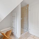 Dusche mit Glaswand, weiße Tür und Heizkörper an der Wand.
