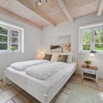 Schlafzimmer mit Doppelbett, Holzdecke, zwei Fenstern und Nachttisch.