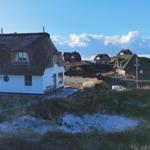 Dorf mit strohgedeckten Häusern auf Hügeln unter blauem Himmel mit weißen Wolken.