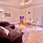 Wohn- und Essbereich mit Sofa, Tisch, Stühlen und Fernseher.
