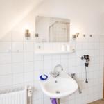 Badezimmer mit Waschbecken, Spiegel und Dusche. Weiße Fliesen und Handtuchhalter.