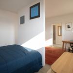Schlafzimmer mit Bett und Tisch. Blick in Wohnbereich mit Schreibtisch und Teppich.