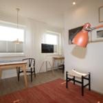 Ein Raum mit Tisch, Stühlen, Fenstern und einer Wandlampe.