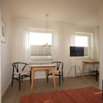 Esszimmer mit Tisch, zwei Stühlen, Fenstern und Fernseher. Holzfußboden und roter Teppich.