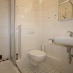 Badezimmer mit Dusche, Toilette und Waschbecken. Fliesenwand und Spiegel.