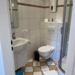 Badezimmer mit Dusche, WC und Waschbecken. Fliesenboden und Spiegel.