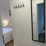 Schlafzimmer mit Bett, Wandspiegel und Hakenwand. Holzboden und weiße Wände.
