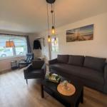 Wohnzimmer mit Sofa, Sessel und Couchtisch. Hängelampe und Wandbild sichtbar.