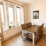 Esszimmer mit Tisch, Stühlen und Fensterfront. Wandbilder und Holzboden.