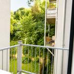 Balkon mit Metallgeländer blickt auf grüne Bäume und einen angrenzenden Balkon.