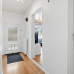 Hausflur mit Holzboden, weißen Wänden und Tür zum Wohnzimmer.