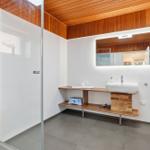 Badezimmer mit Dusche, Waschbecken und Toilette. Holzdecke und -möbel.
