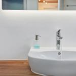Waschbecken mit laufendem Wasser, Seifenspender und Spiegel im Badezimmer.