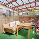 Terrassenbereich mit Sofa, Tisch und Stühlen unter Glasdach.