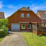 Rotes Backsteingebäude mit Garage und Gartenhaus. Grünflächen und gepflasterter Weg.