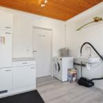 Wohnraum mit Waschmaschine, Spüle und Trockner. Holzdecke und weiße Möbel.