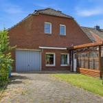 Rotes Backsteingebäude mit Garage und Holzveranda. Grasfläche und Kiesweg.