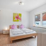 Schlafzimmer mit Holzbett, Kleiderschrank und Fenster mit Blick auf Gebäude.