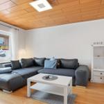Wohnzimmer mit grauem Sofa, weißem Couchtisch und Holzdecke.