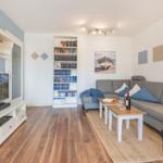 Wohnzimmer mit Sofa, Bücherregal, Fernseher und Holzboden.