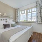 Schlafzimmer mit weißem Bett, Fenster mit Vorhängen und Holzboden.