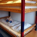 Ein Doppelstockbett mit Holzgestell und roten Säulen. Auf dem unteren Bett liegen zwei Plüschtiere.