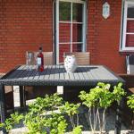Terrasse mit Tisch, Stühlen und einer Flasche. Hintergrund: rote Backsteinwand und Fenster.
