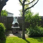 Garten mit Grill, Bäumen und Hecke. Hintergrund zeigt ein Haus.