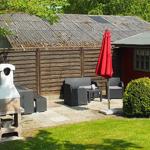 Roter Gartenhäuschen mit Terrasse, Grill und Sitzmöbel unter rotem Sonnenschirm.