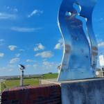 Metallskulptur auf Betonsockel mit Blick auf Grünfläche und Himmel