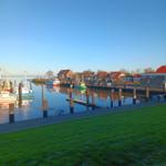 Hafen mit Booten, grüner Rasen und Häusern am Wasser.