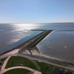 Panoramablick auf einen Deich mit Wasser und Grünflächen im Vordergrund.