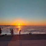 Sonnenuntergang am Strand mit Menschen, die im Wasser stehen und sich entspannen.