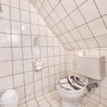Badezimmer mit Toilette, WC und Abflussrohr. Wände und Boden sind mit Fliesen ausgelegt.