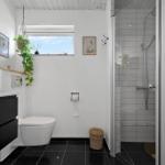 Badezimmer mit Dusche, Toilette und Waschmaschine. Schwarze Fliesen und weiße Wände.